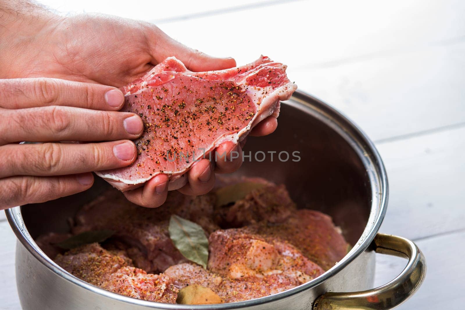 Close up of chefs hands spicing the meat. Casserole with raw meat on a white background.