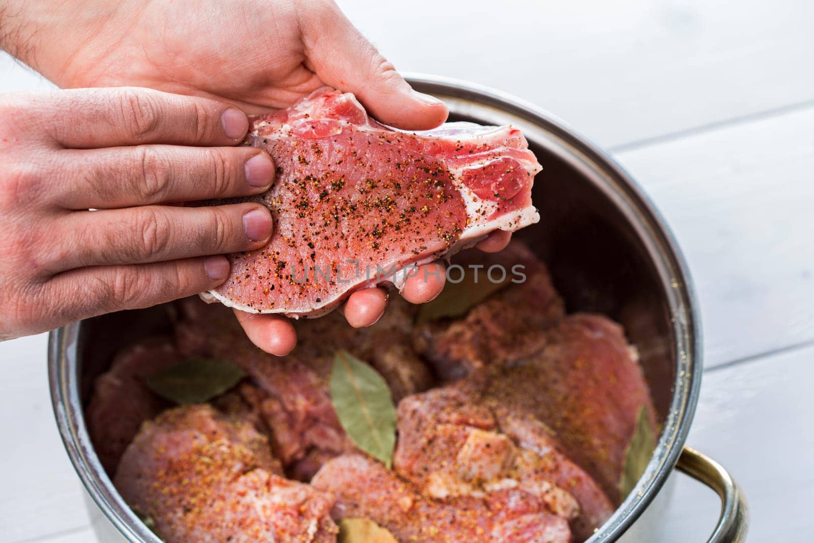 Close up of chefs hands spicing the meat. Casserole with raw meat on a white background.