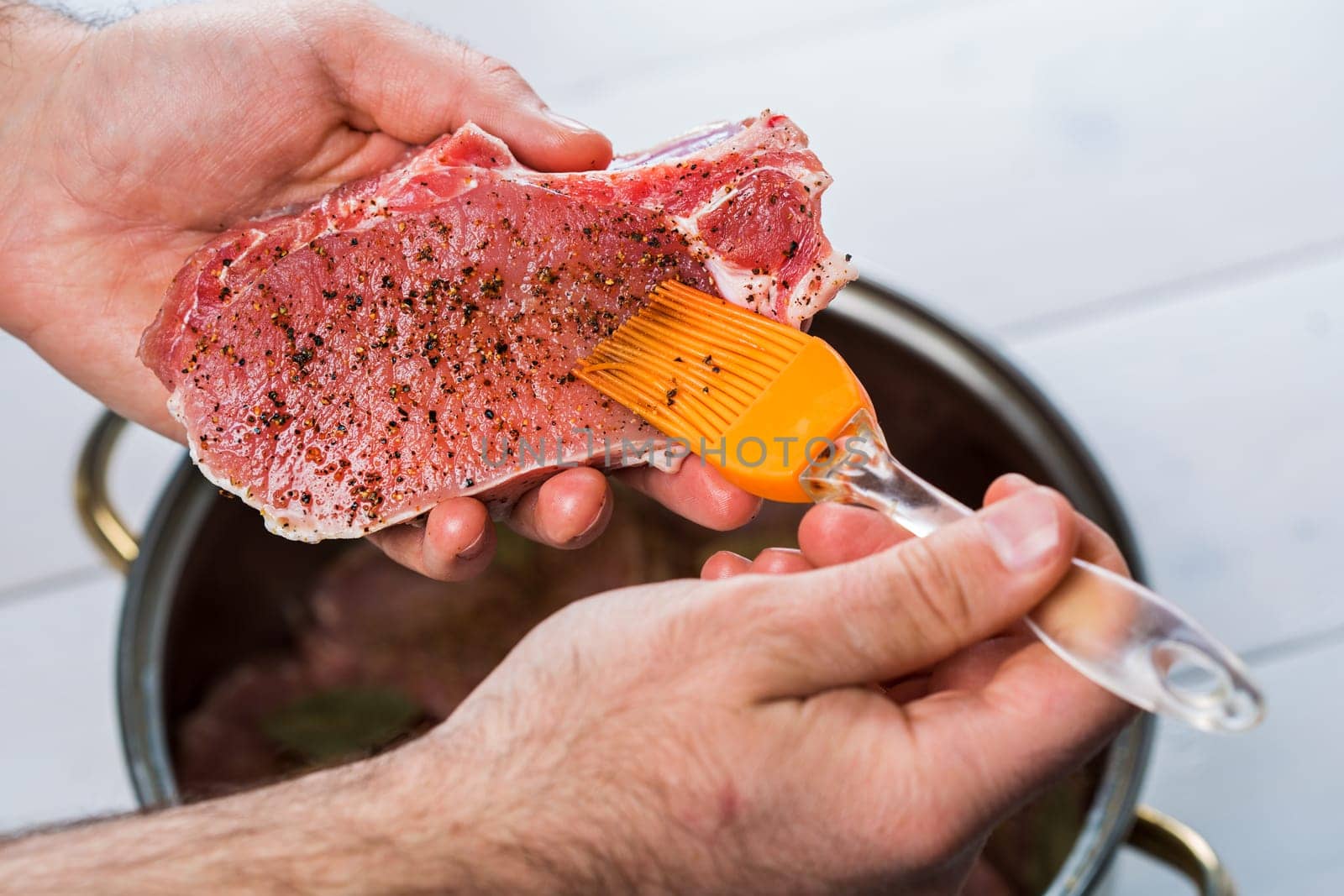 Close up of chefs hands spicing the meat. Casserole with raw meat on a white background.