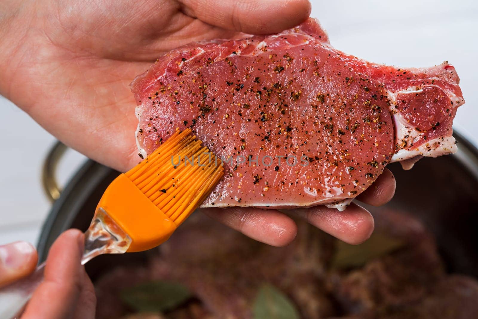 Close up of chefs hands spicing the meat. Casserole with raw meat on a white background.