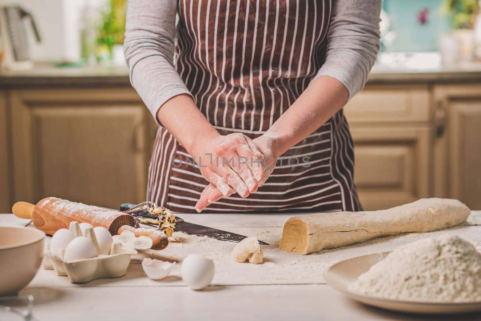 Woman bake pies. Confectioner makes desserts. Making buns. Dough on the table. Knead the dough. A woman in a striped apron is cooking in the kitchen