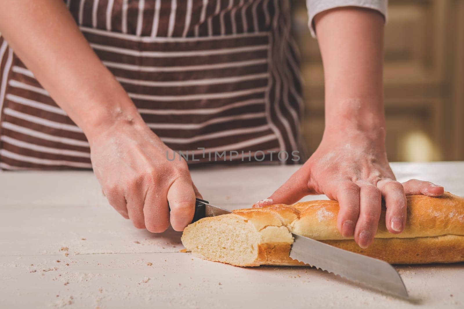 Woman cutting bread on wooden board. Bakehouse. Bread production. A woman in a striped apron