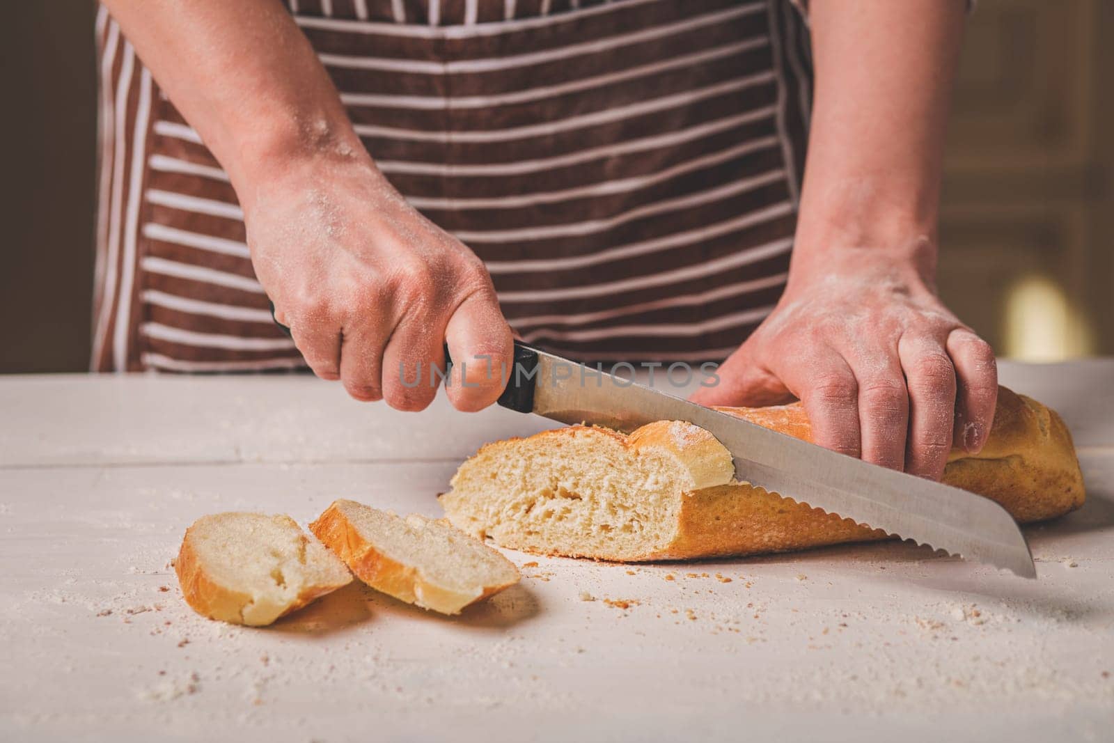 Woman cutting bread on wooden board. Bakehouse. Bread production. A woman in a striped apron