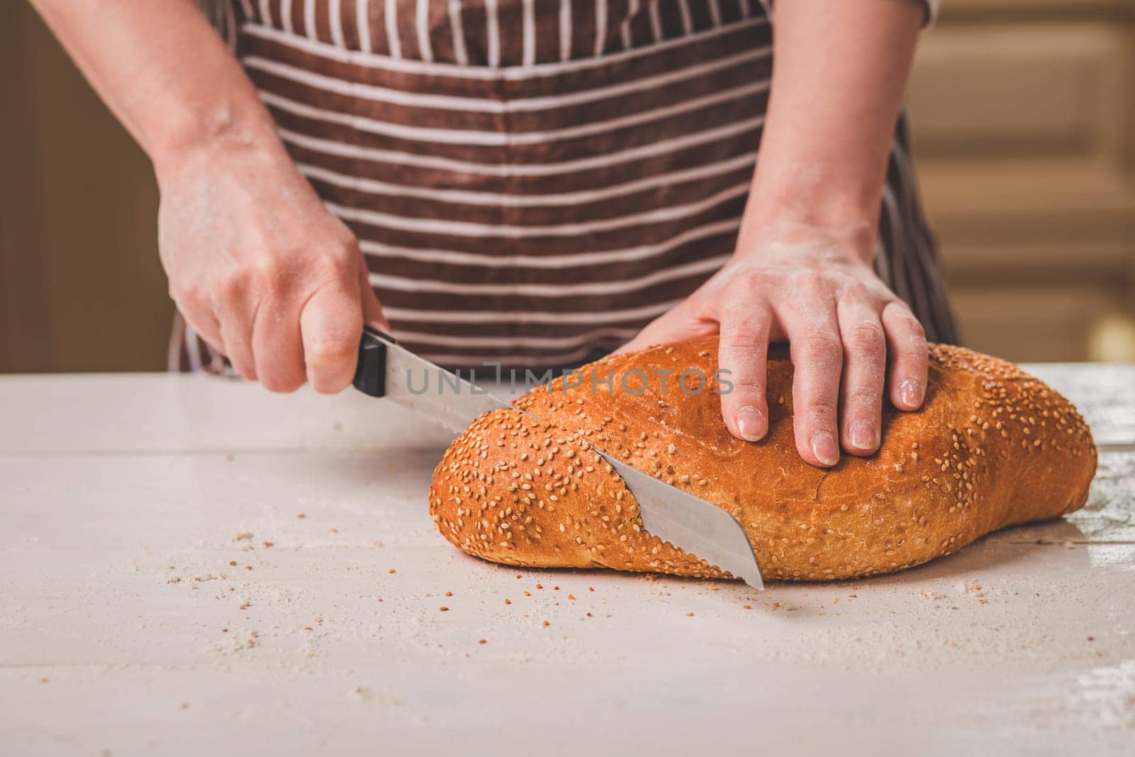 Woman cutting bread on wooden board. Bakehouse. Bread production. A woman in a striped apron