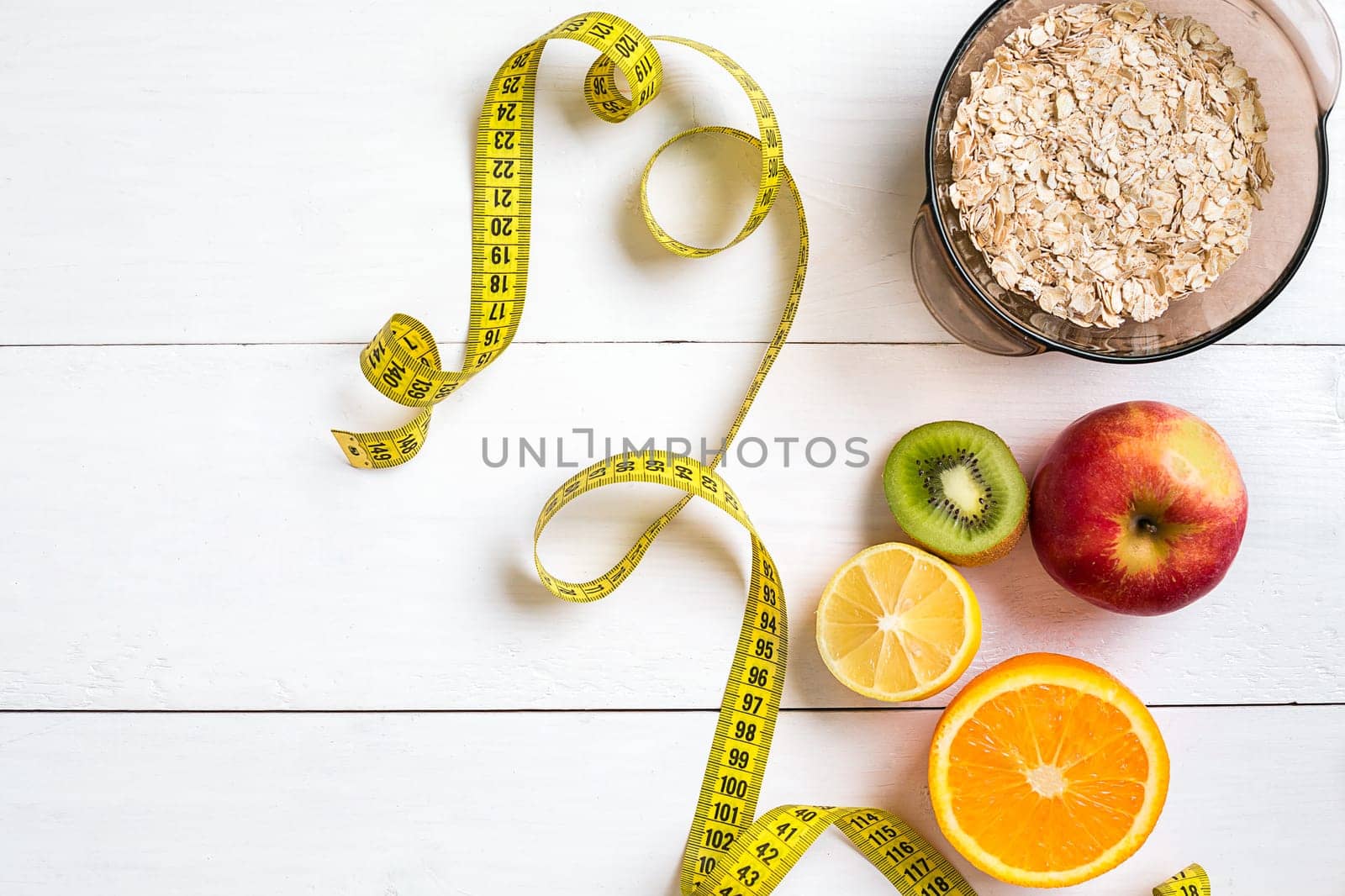 Fitness concept with fruit, bowl of oatmeal and centimeter. Top view background concept. Copy space