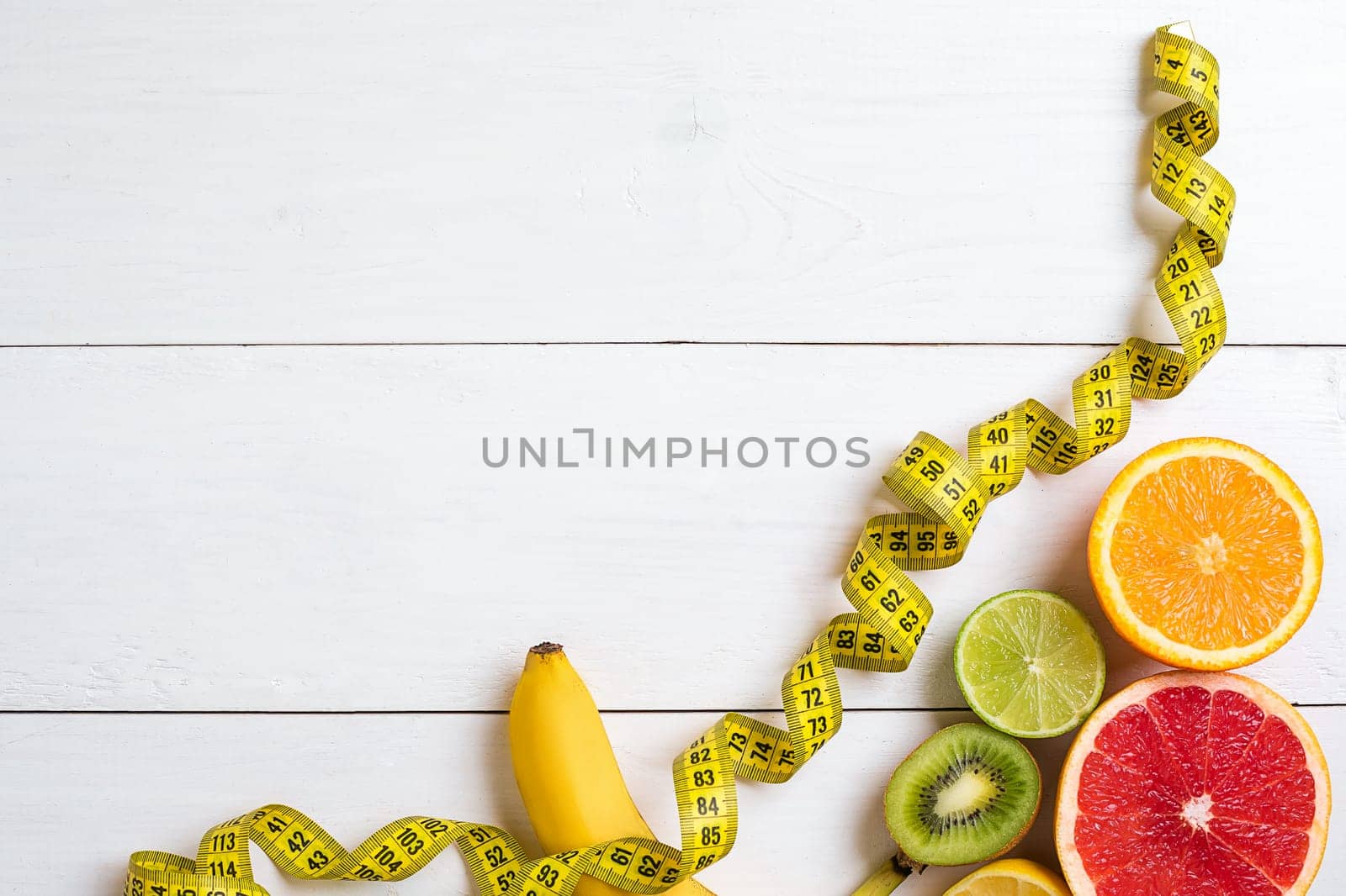 Fresh fruits with tape measure over white wooden background. Fitness concept. Top view. Copy space Flat lay