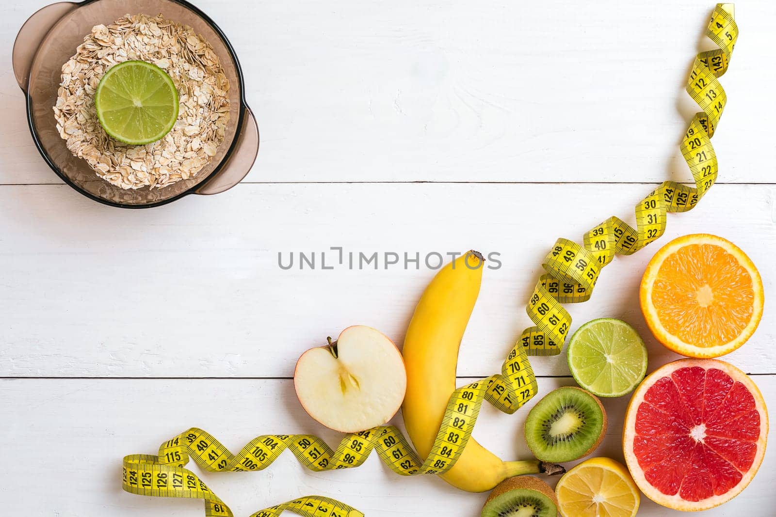 Fresh fruits with tape measure over white wooden background. Fitness concept. Top view. Copy space Flat lay