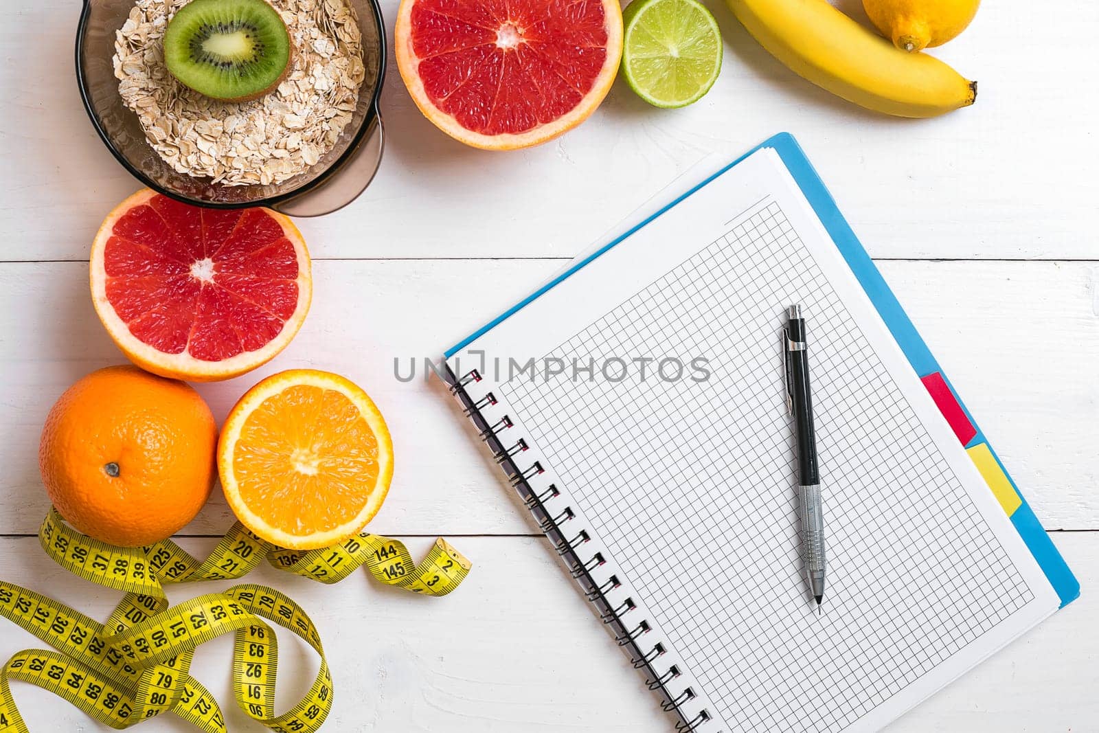 Healthy breakfast with oatmeal, fresh fruits and notebook on rustic wooden table. Top view.