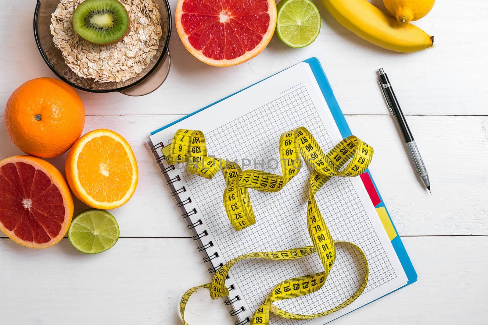 Healthy breakfast with oatmeal, fresh fruits and notebook on rustic wooden table. Top view.
