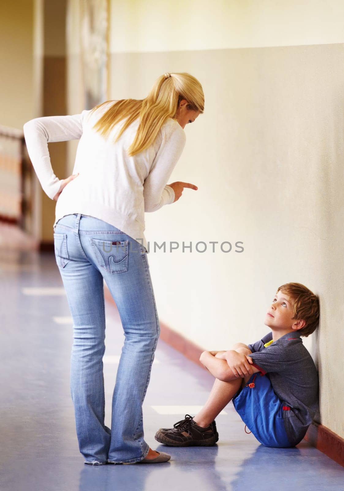 Teacher, student and scolding child at school for bad behaviour, problem or attitude. Angry woman pointing and talking to punish naughty boy for discipline, lesson or education fail in hallway by YuriArcurs