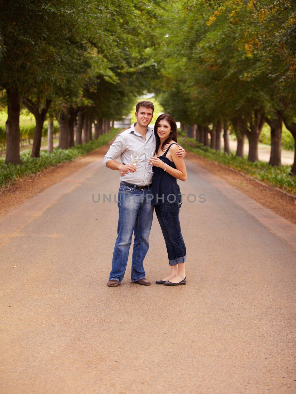 Couple, portrait and wine outdoor at a vineyard for vacation, holiday or travel with love and care. Man and a woman hug on a countryside road with trees, alcohol glass or drinks to celebrate marriage.