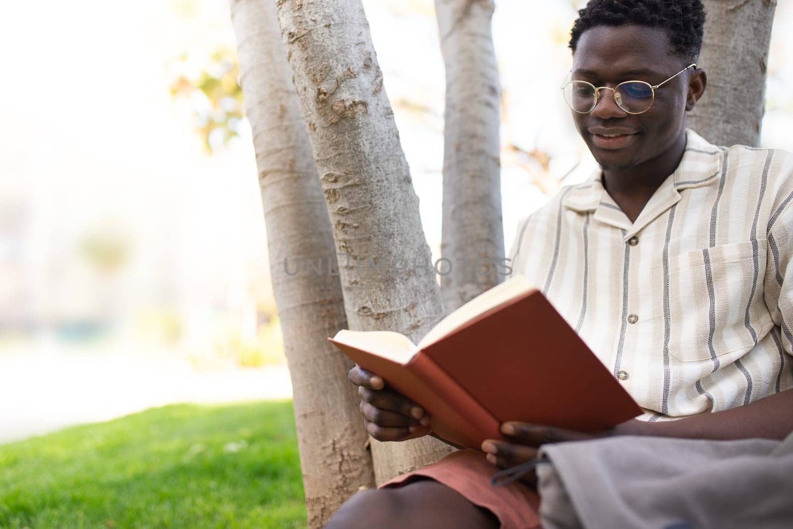 African american college student reading book on campus. Young black man reading book outdoors. Copy space. Education concept.