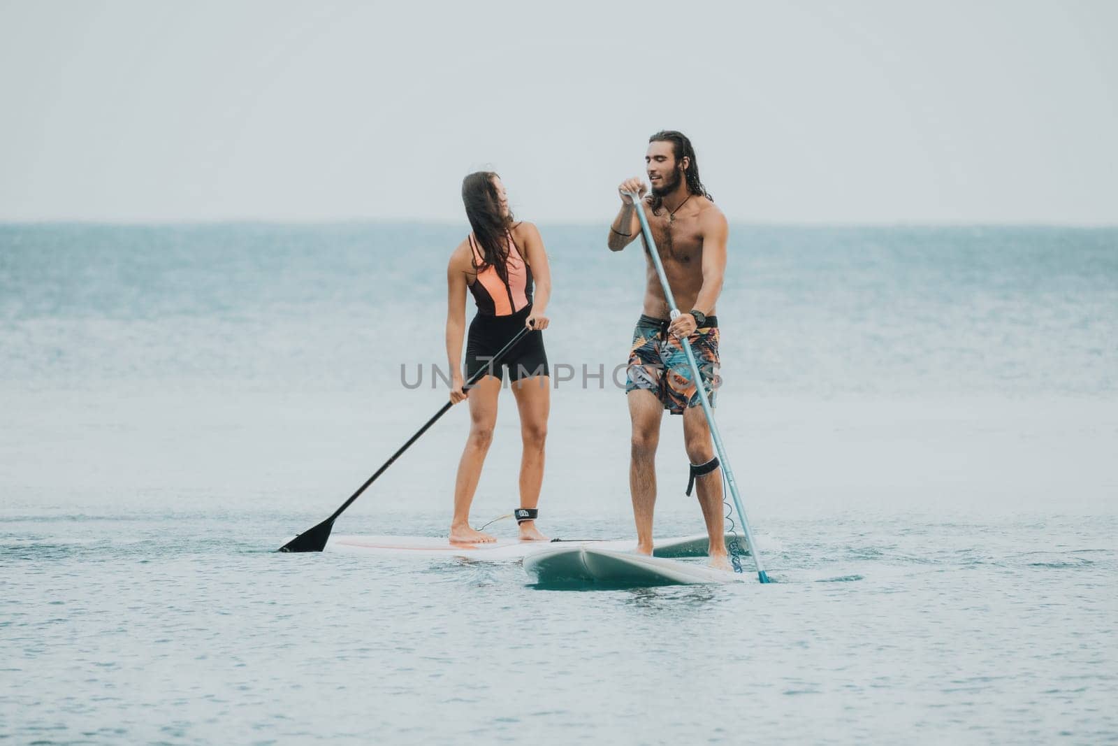 Sea woman and man on sup. Silhouette of happy young woman and man, surfing on SUP board, confident paddling through water surface. Idyllic sunset. Active lifestyle at sea or river