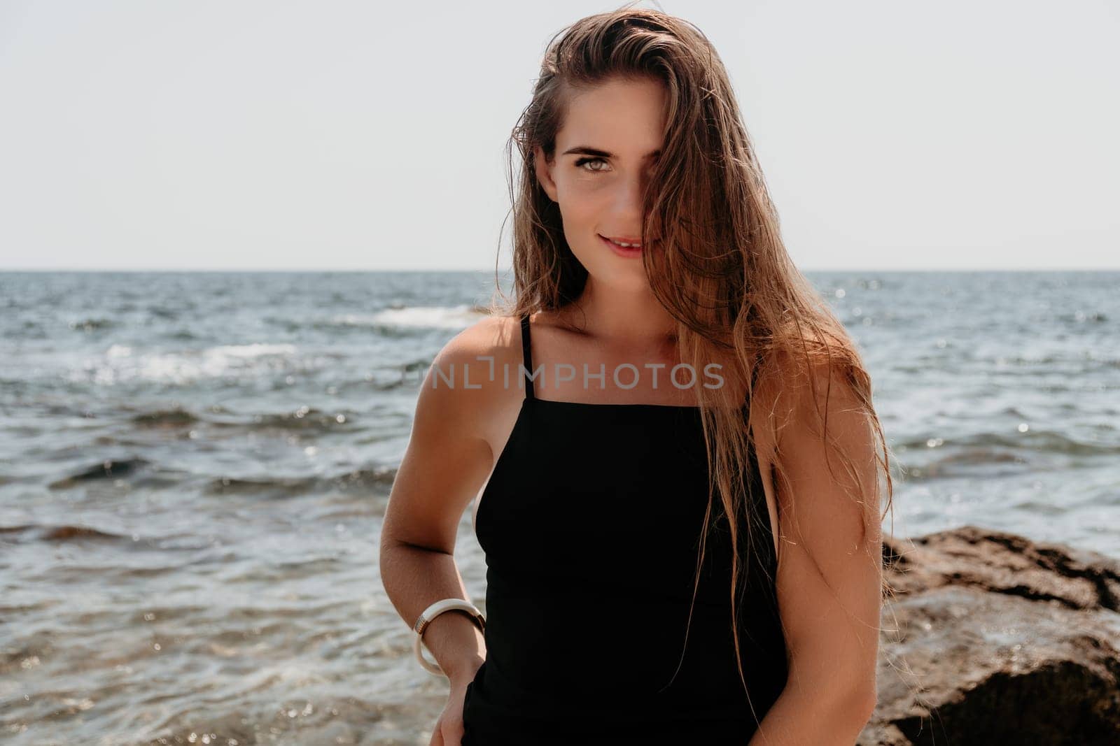 Woman travel sea. Young Happy woman in a long red dress posing on a beach near the sea on background of volcanic rocks, like in Iceland, sharing travel adventure journey