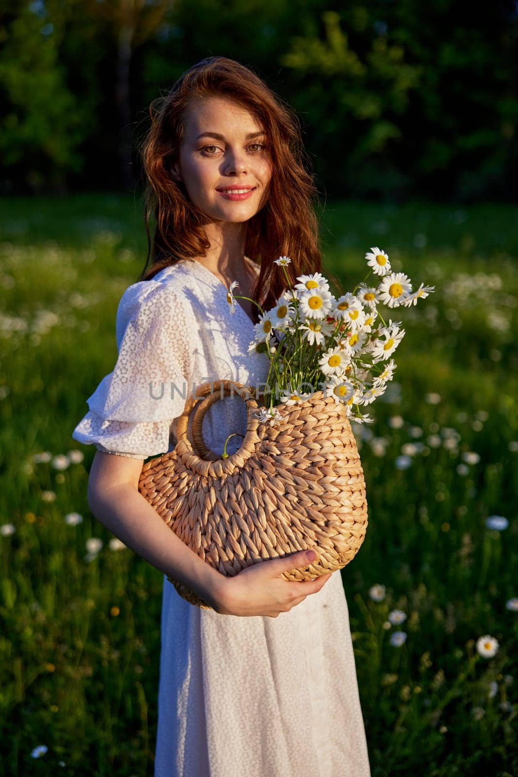 portrait of a beautiful red-haired girl in a light summer dress in nature with a basket of flowers. High quality photo