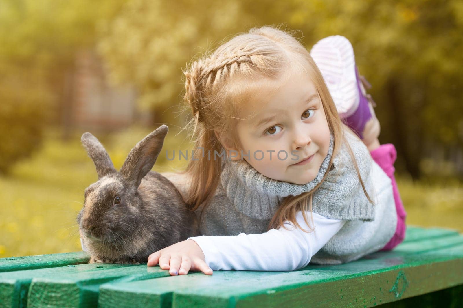 Cute brown-eyed girl lying on bench with rabbit, close-up