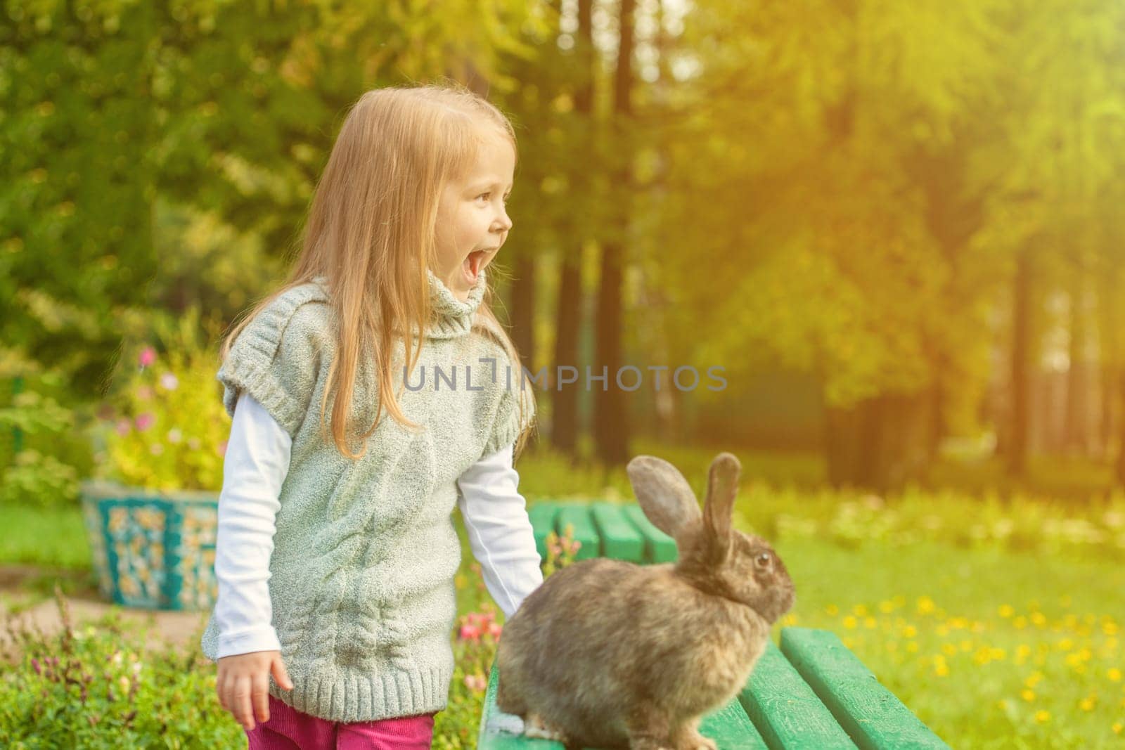 Cheerful little girl walking with rabbit in park, close-up