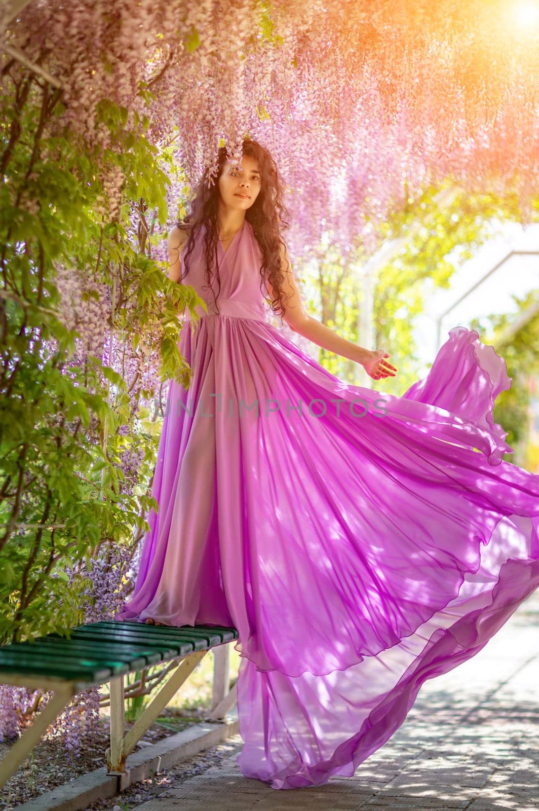 Woman wisteria lilac dress. Thoughtful happy mature woman in purple dress surrounded by chinese wisteria.