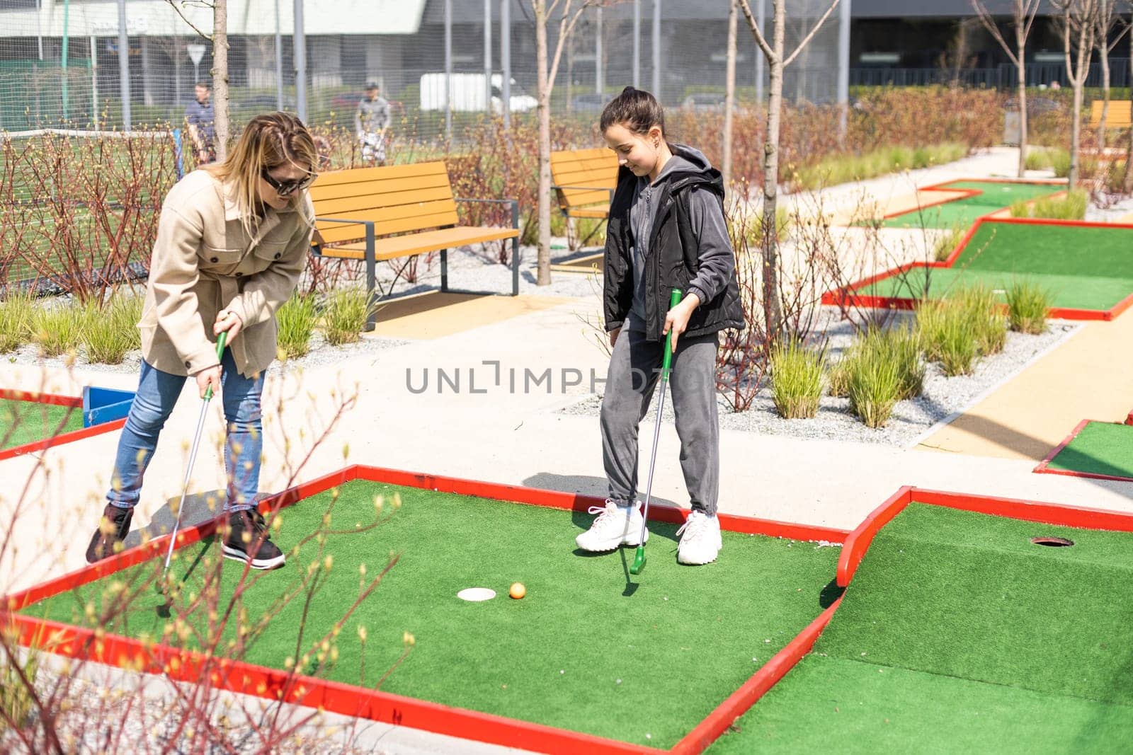 mother and daughter enjoying together playing mini golf in the city