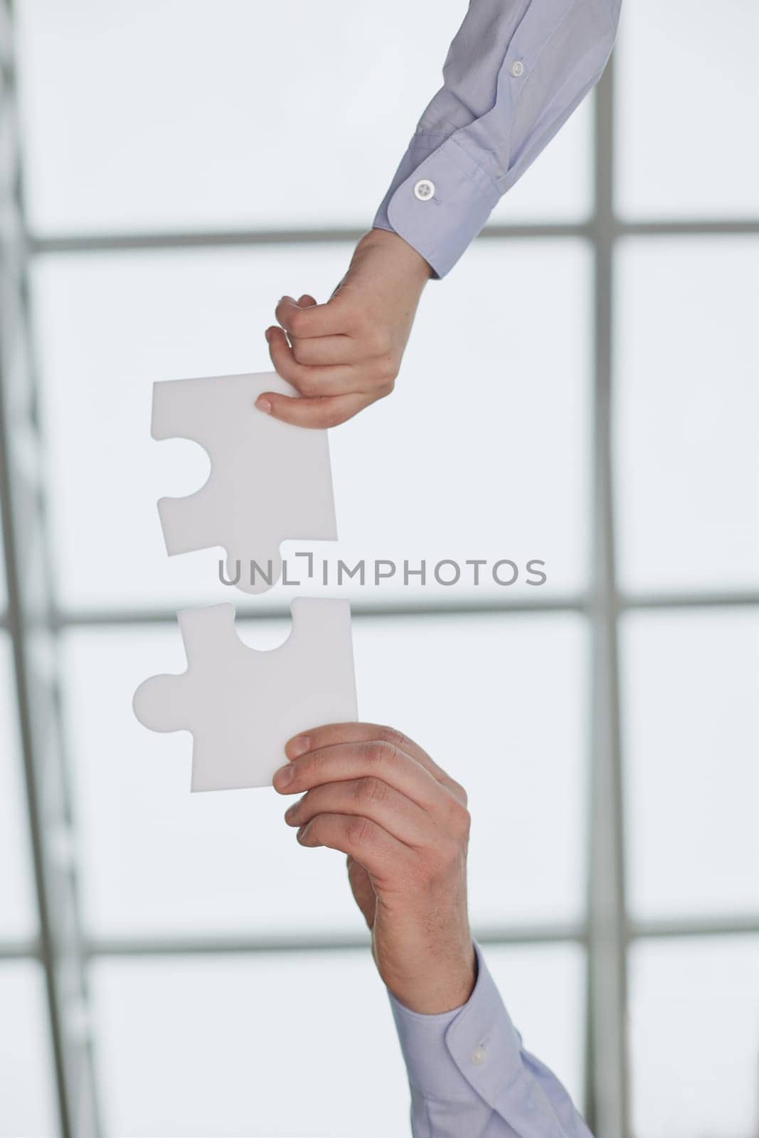 Putting the pieces together. an unidentifiable businesswoman holding two puzzle pieces together in the office.