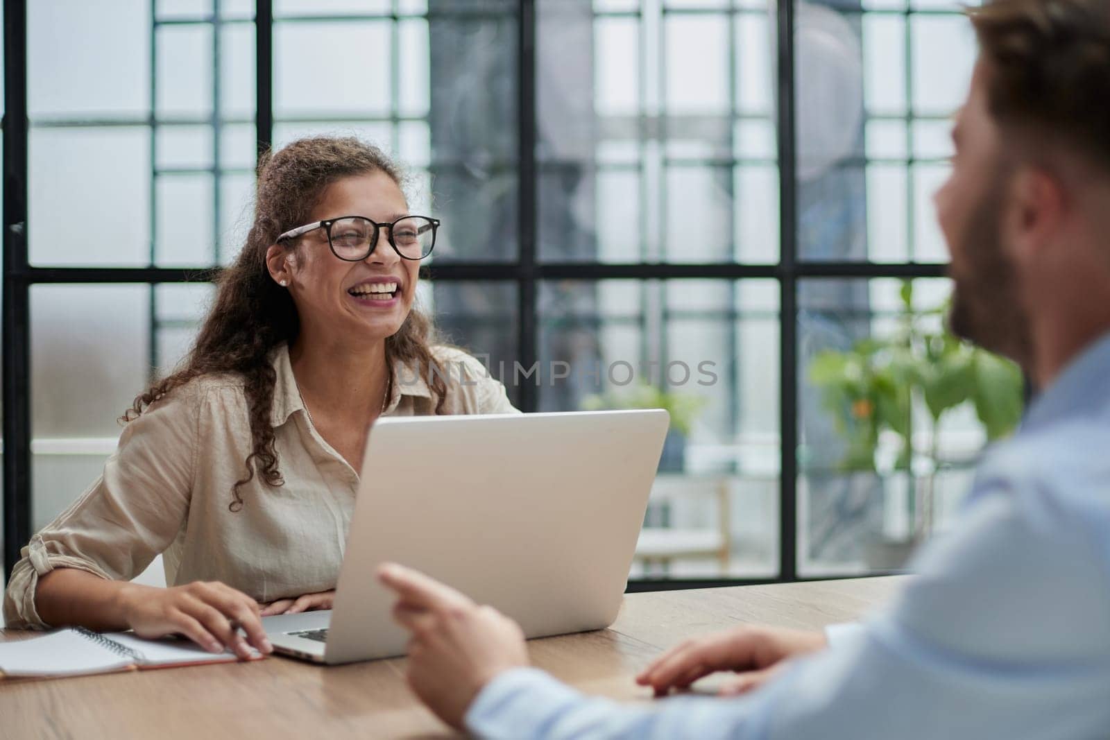 manager in glasses sitting at the table receives a client in the office looking at the camera