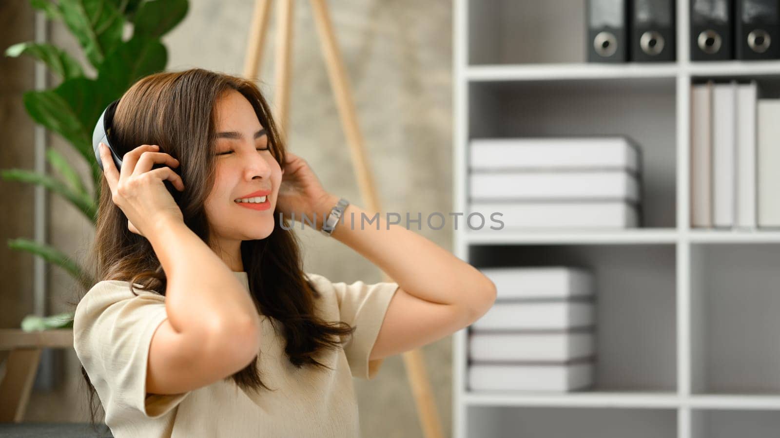 Relaxed young woman listening to favorite music on wireless headphone with closed eyes by prathanchorruangsak