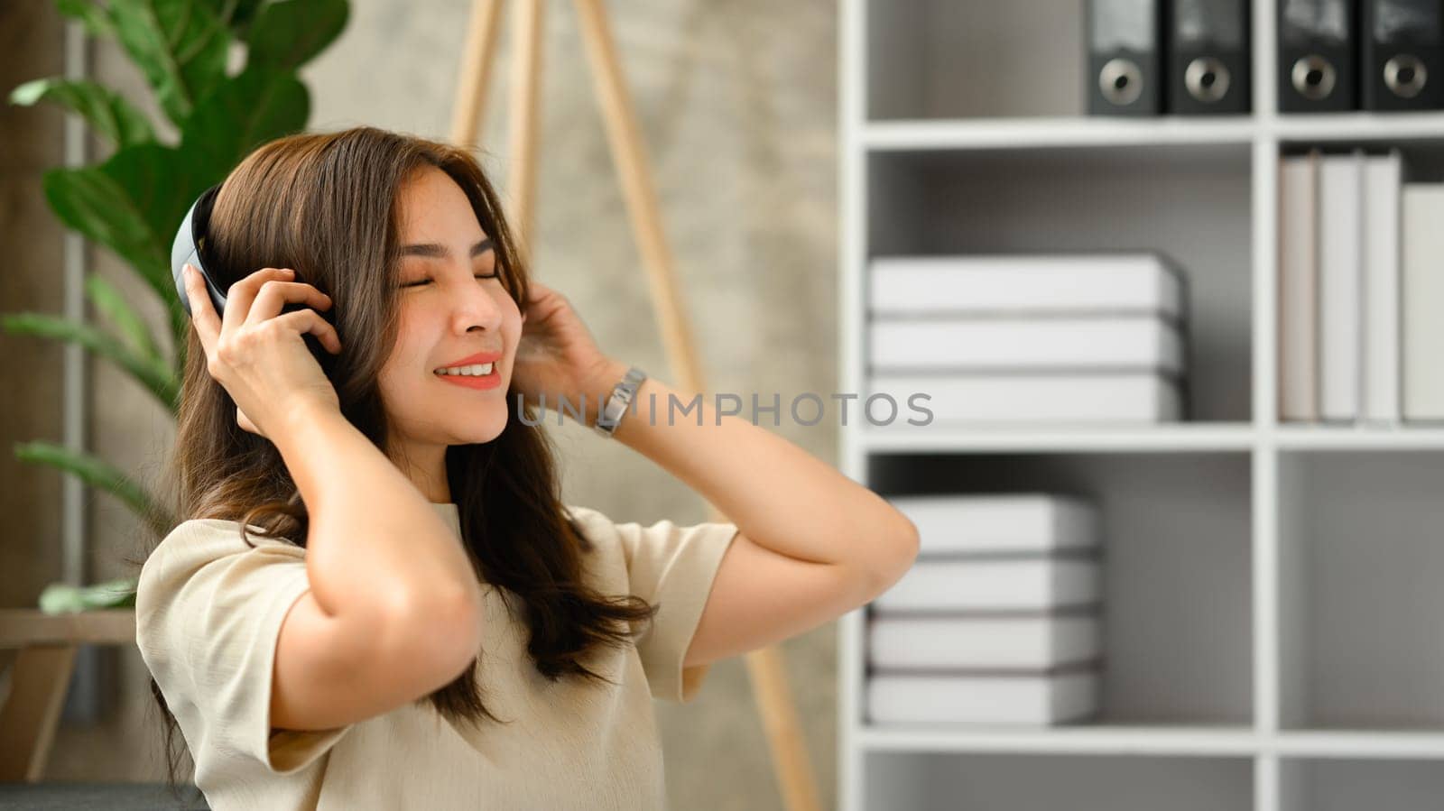 Relaxed young woman listening to favorite music on wireless headphone with closed eyes.