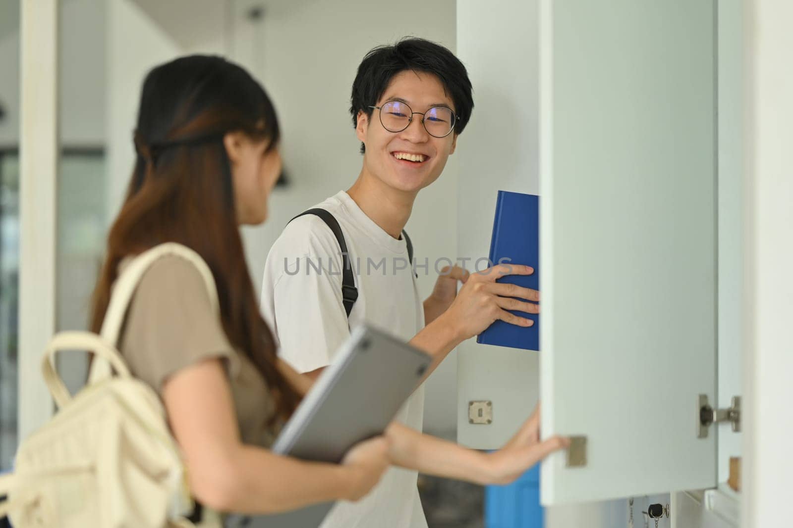 Two young college friends talking while standing at lockers in campus hallway. Education, Learning and technology concept by prathanchorruangsak