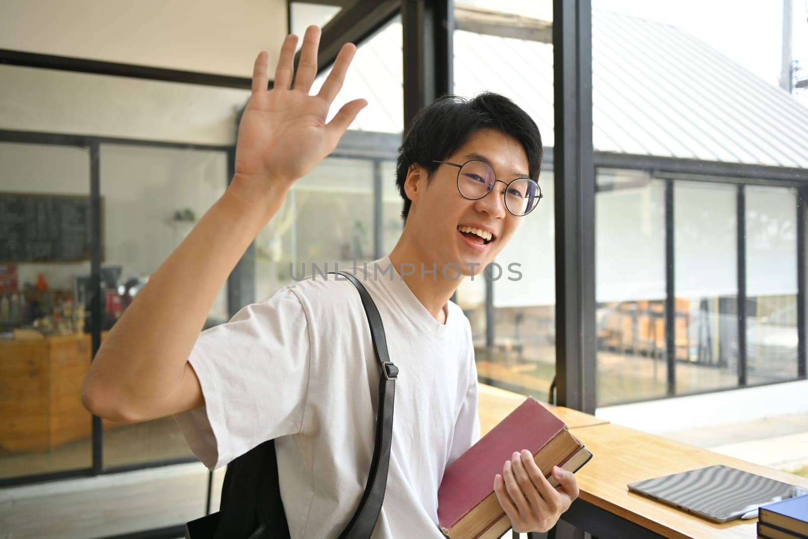Shot of young man student waving hand for greeting to his friend in university campus by prathanchorruangsak
