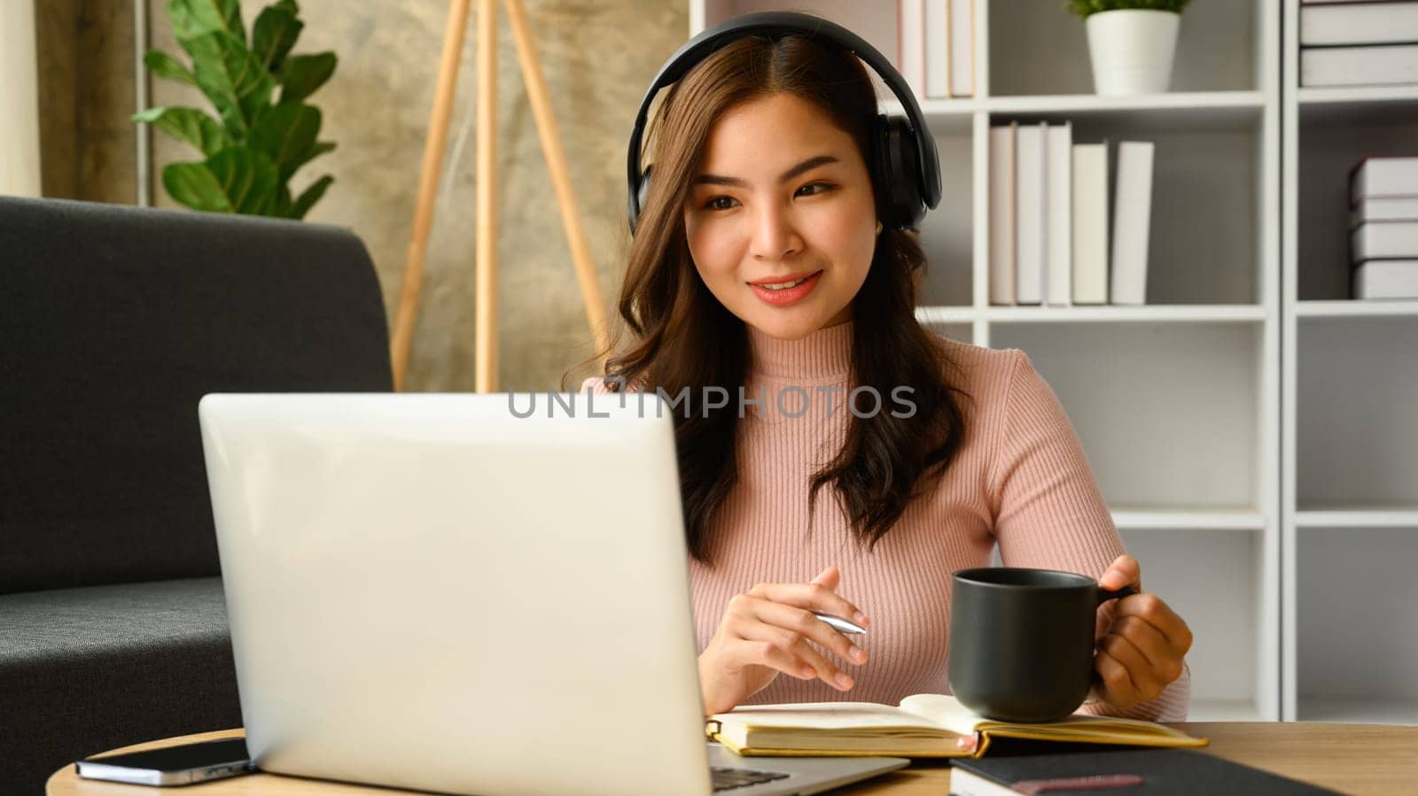 Attractive female student with wireless headphone learning distantly, watching online lecture on laptop screen.