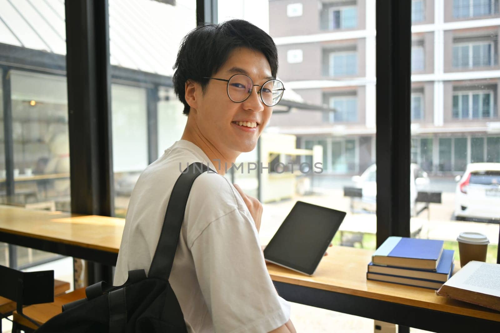 Portrait of smiling college student distantly working or studying on laptop, using free wifi in coffee shop.