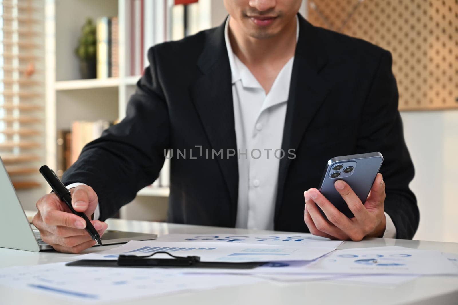 Young start up businessman using smartphone and checking marketing report at work desk.