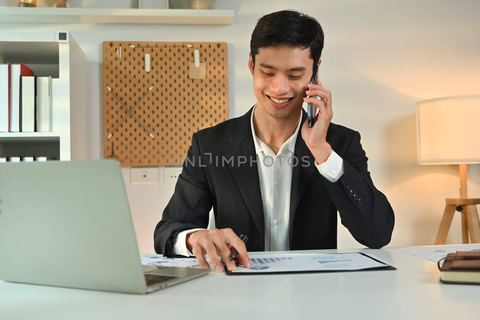 Successful businessman sitting behind a laptop and talking on mobile phone. People, communication, technology by prathanchorruangsak