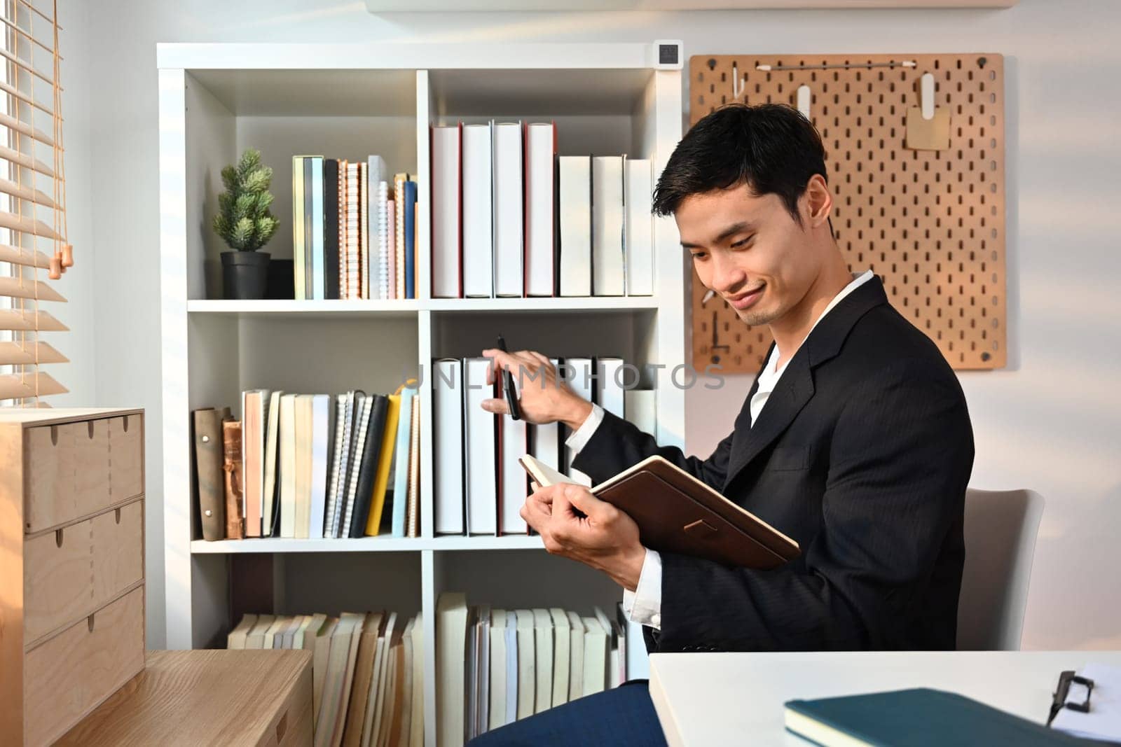 Handsome young businessman reading notes in planner or checking his working schedule plan at workplace.