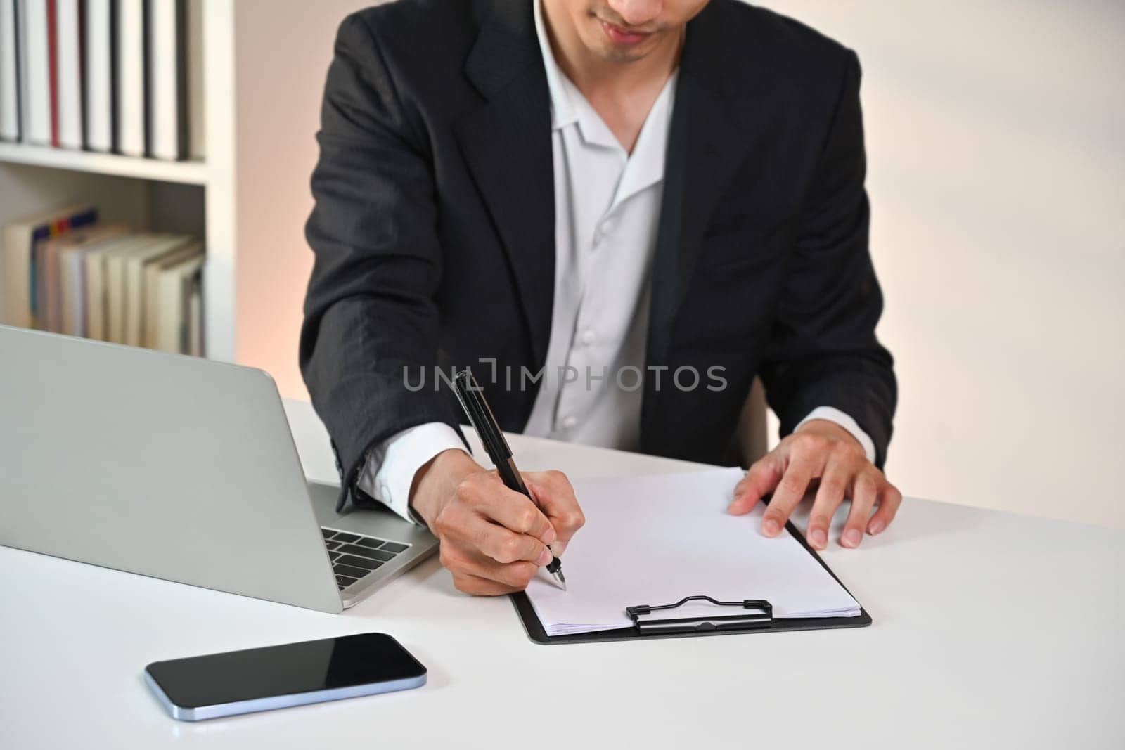 Businessman manager holding pen writing on documents, checking marketing report at desk.