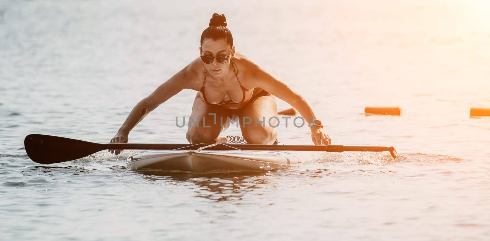 Sea woman sup. Silhouette of happy middle aged woman in rainbow bikini, surfing on SUP board, confident paddling through water surface. Idyllic sunset. Active lifestyle at sea or river