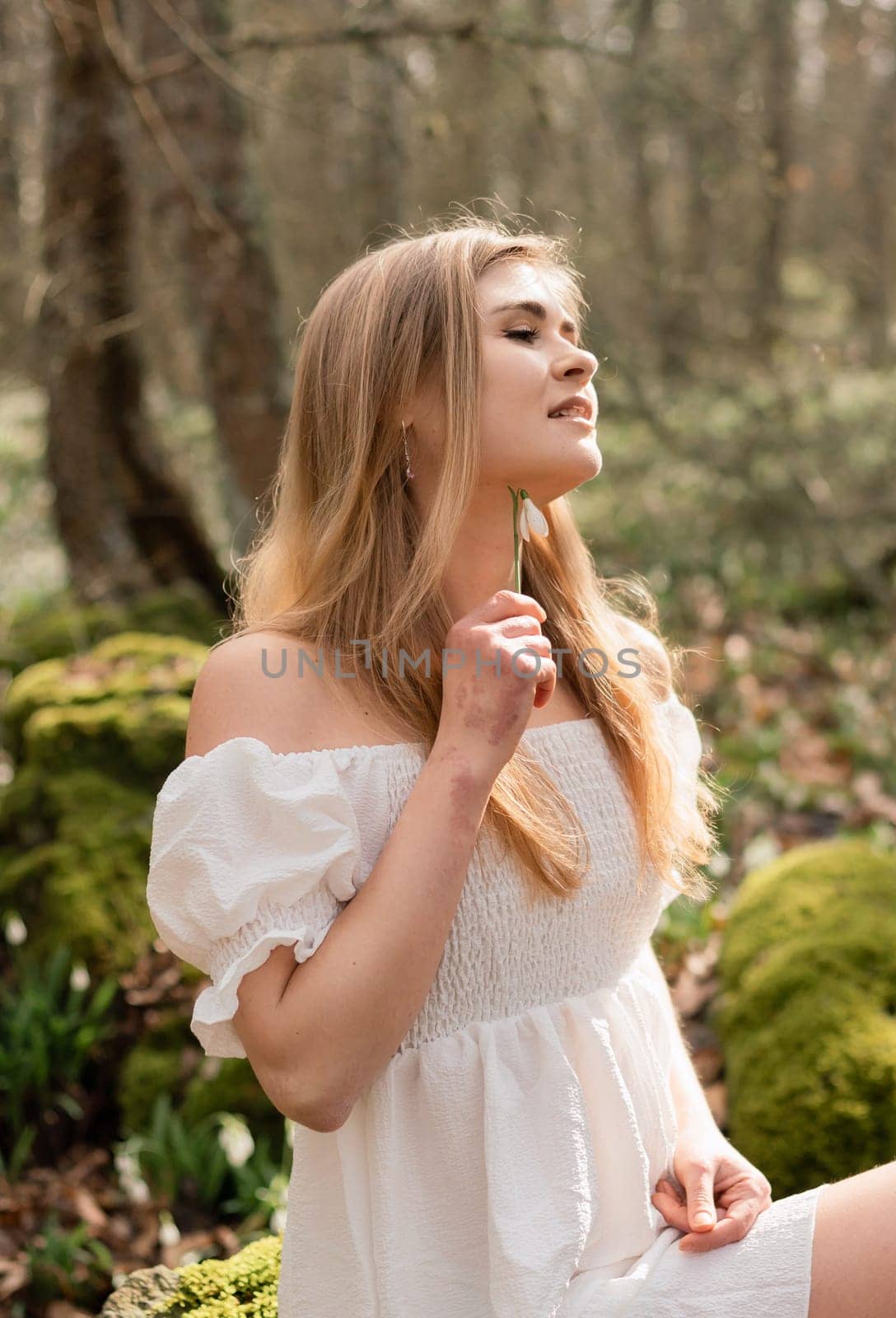 Snowdrops galanthus blonde. A girl in a white dress sits on a meadow with snowdrops in a spring forest by Matiunina