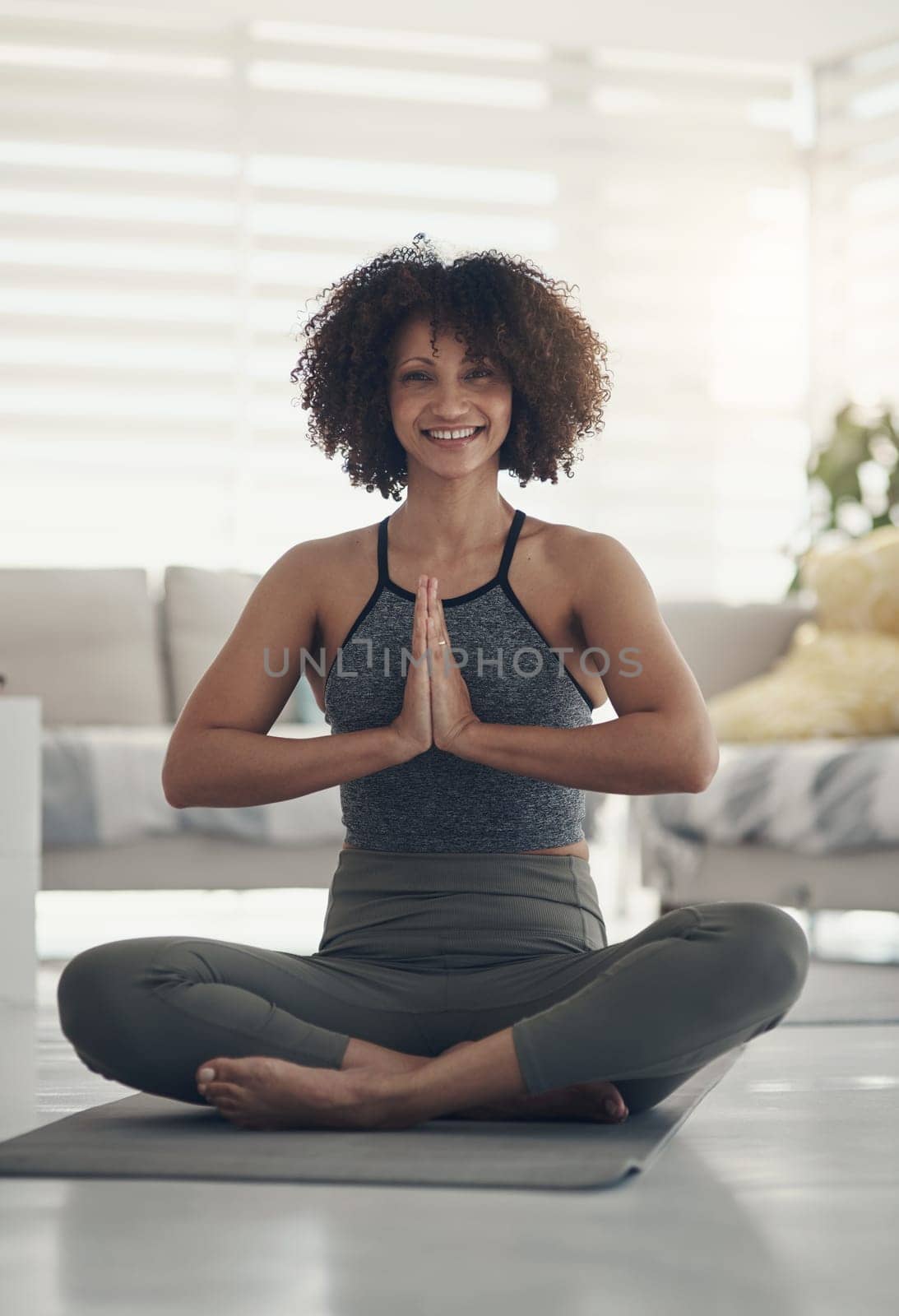 Thanking my body for this practice. Full length shot of an attractive young woman sitting alone in her living room and meditating. by YuriArcurs