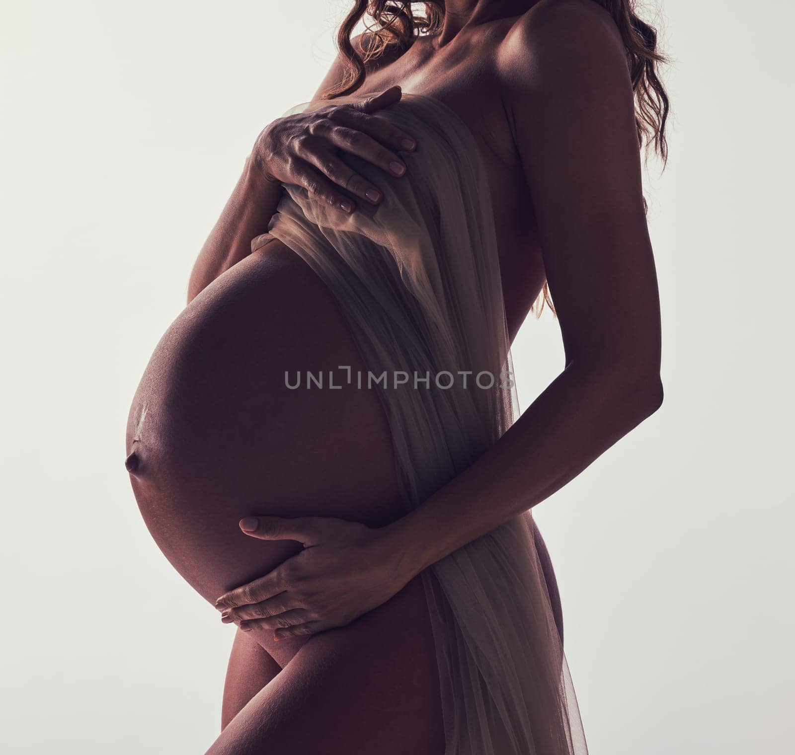 Woman, pregnant and fabric on stomach in studio with hands, touch and art by white background. Pregnancy model, shadow and mom wellness with cloth for body, belly and silhouette with dark aesthetic by YuriArcurs