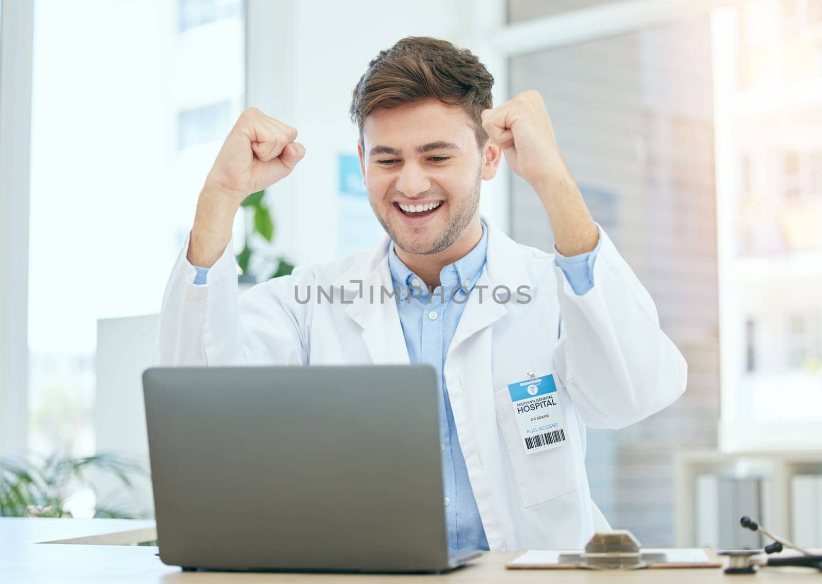Success, medical and laptop with doctor in hospital and cheering for celebration, report or achievement. Winner, research and technology with man reading good news for healthcare, medicine or science.