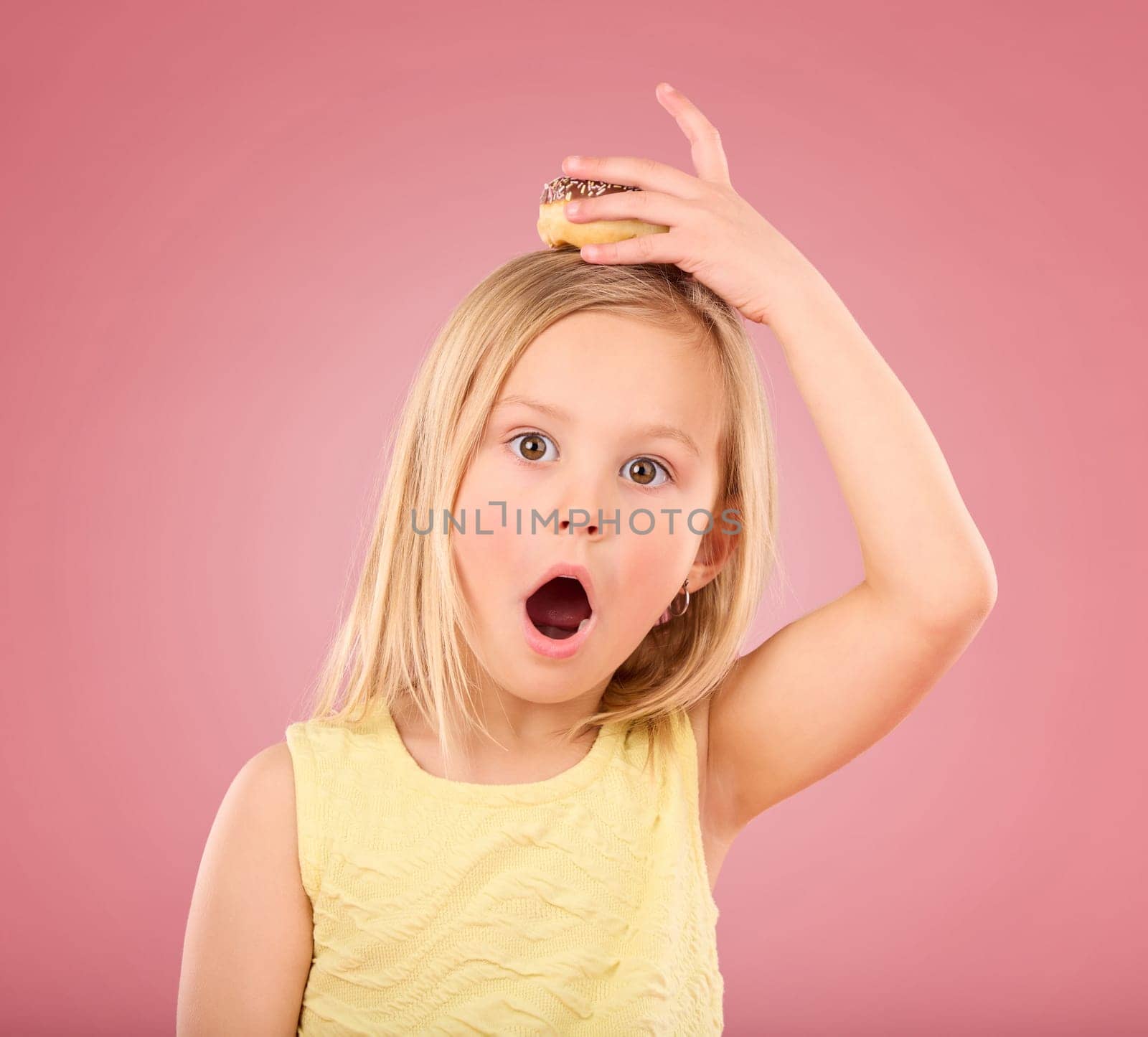 Child, donut and wow face portrait in studio with hand on head on a pink background. Girl kid model with sweet snack, surprise and shocked or comic expression isolated on creative color and space.