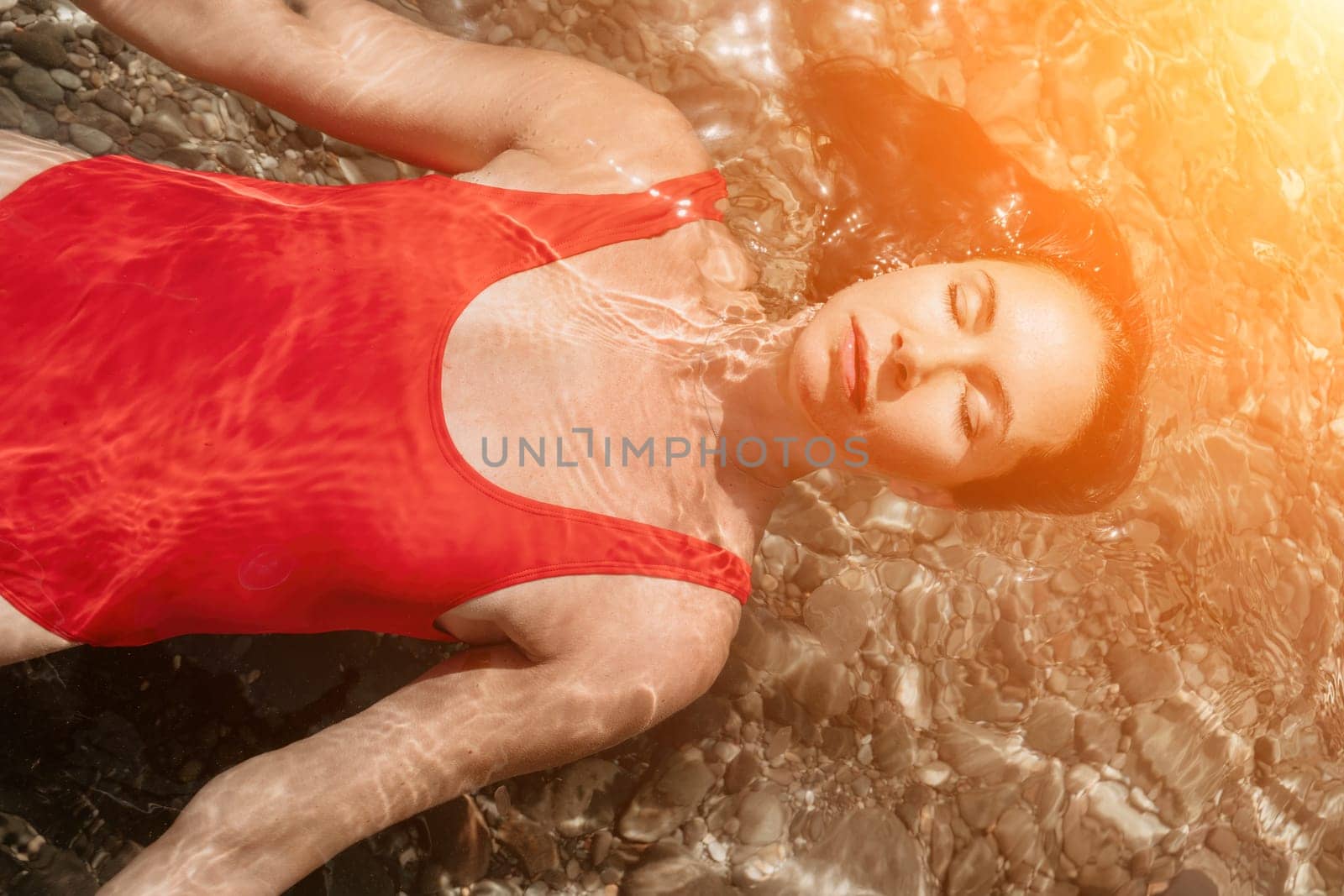 Woman travel portrait. Close-up portrait of a happy woman with long hair in a red bikini, floating in water and smiling at the camera. by panophotograph