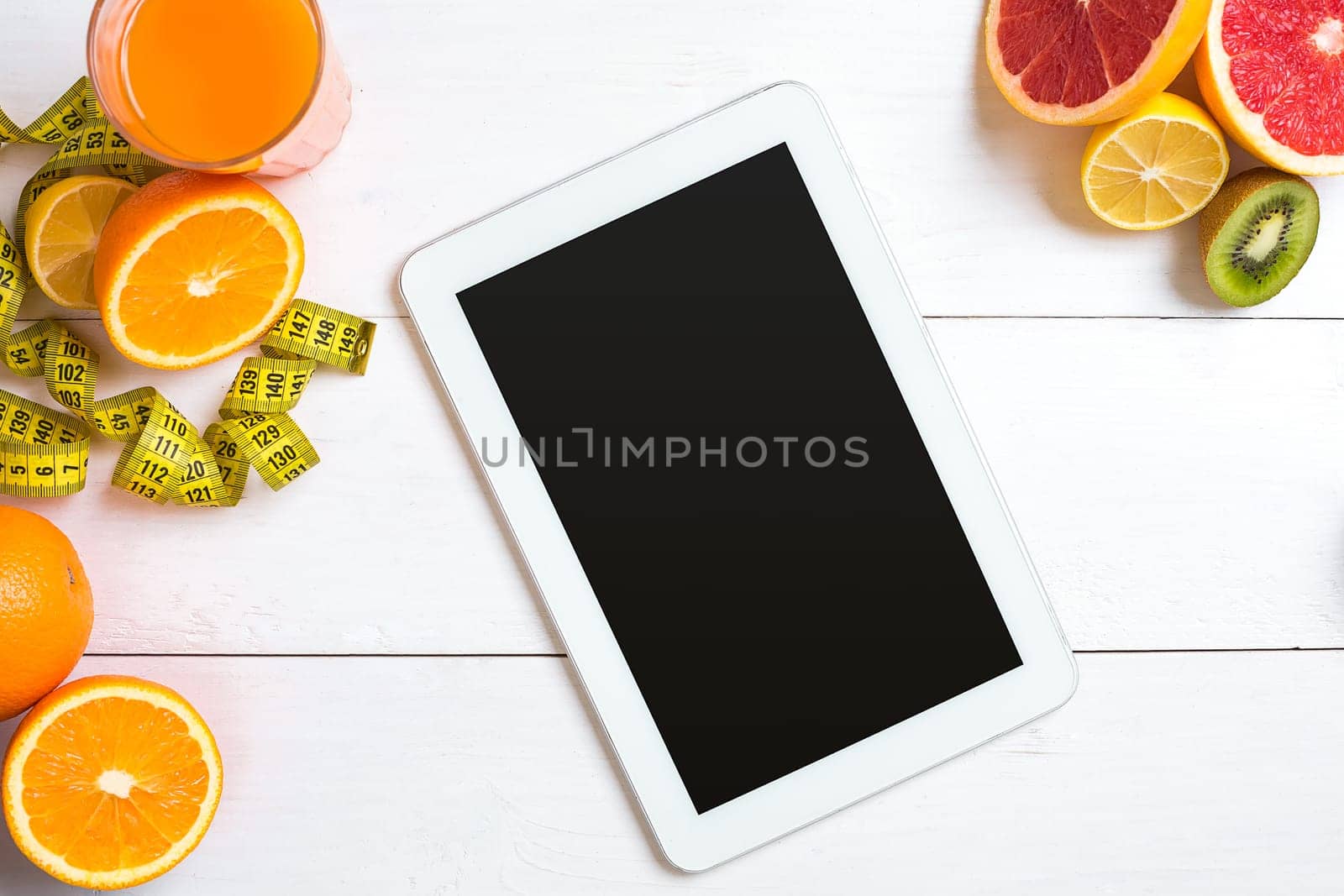 Fresh juice in glass from citrus fruits - lemon, grapefruit, orange on white wooden background, top view. White tablet with copy space