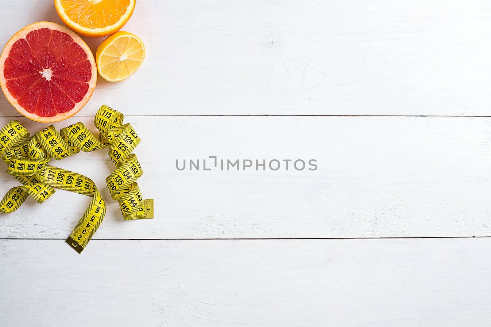Fresh fruits with tape measure over white wooden background. Fitness concept. Top view. Copy space Flat lay