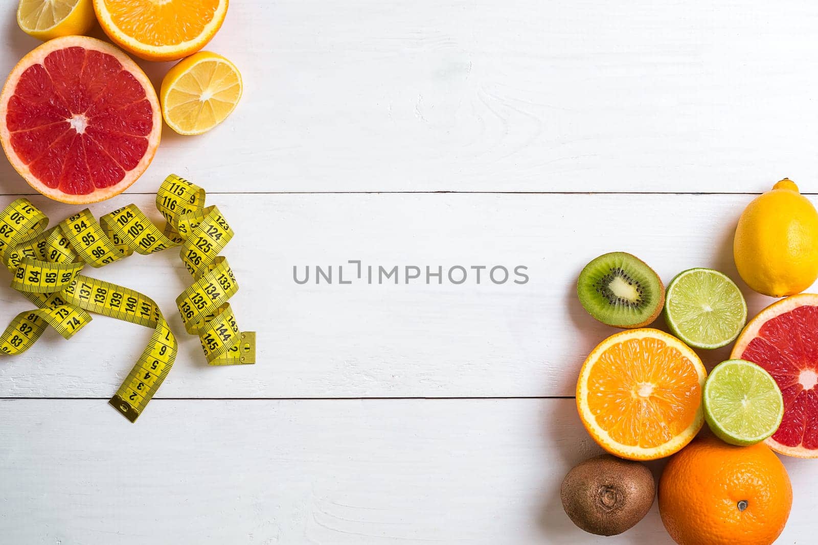 Fresh fruits with tape measure over white wooden background. Fitness concept. Top view. Copy space Flat lay