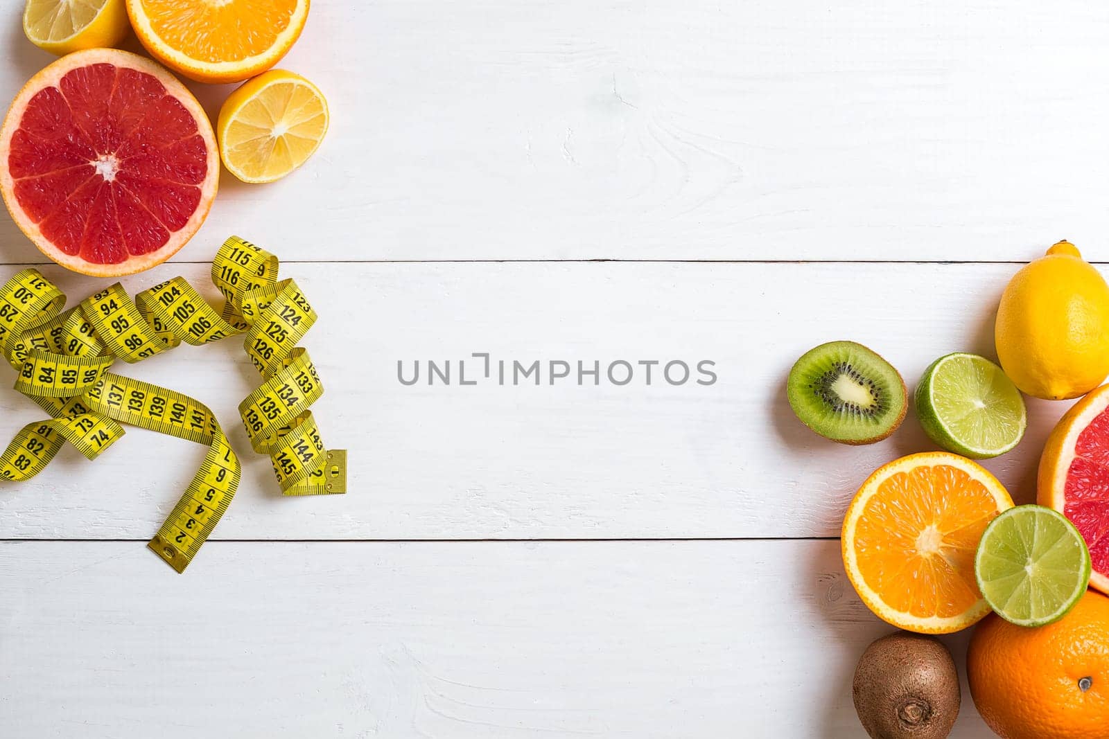 Fresh fruits with tape measure over white wooden background. Fitness concept. Top view. Copy space Flat lay