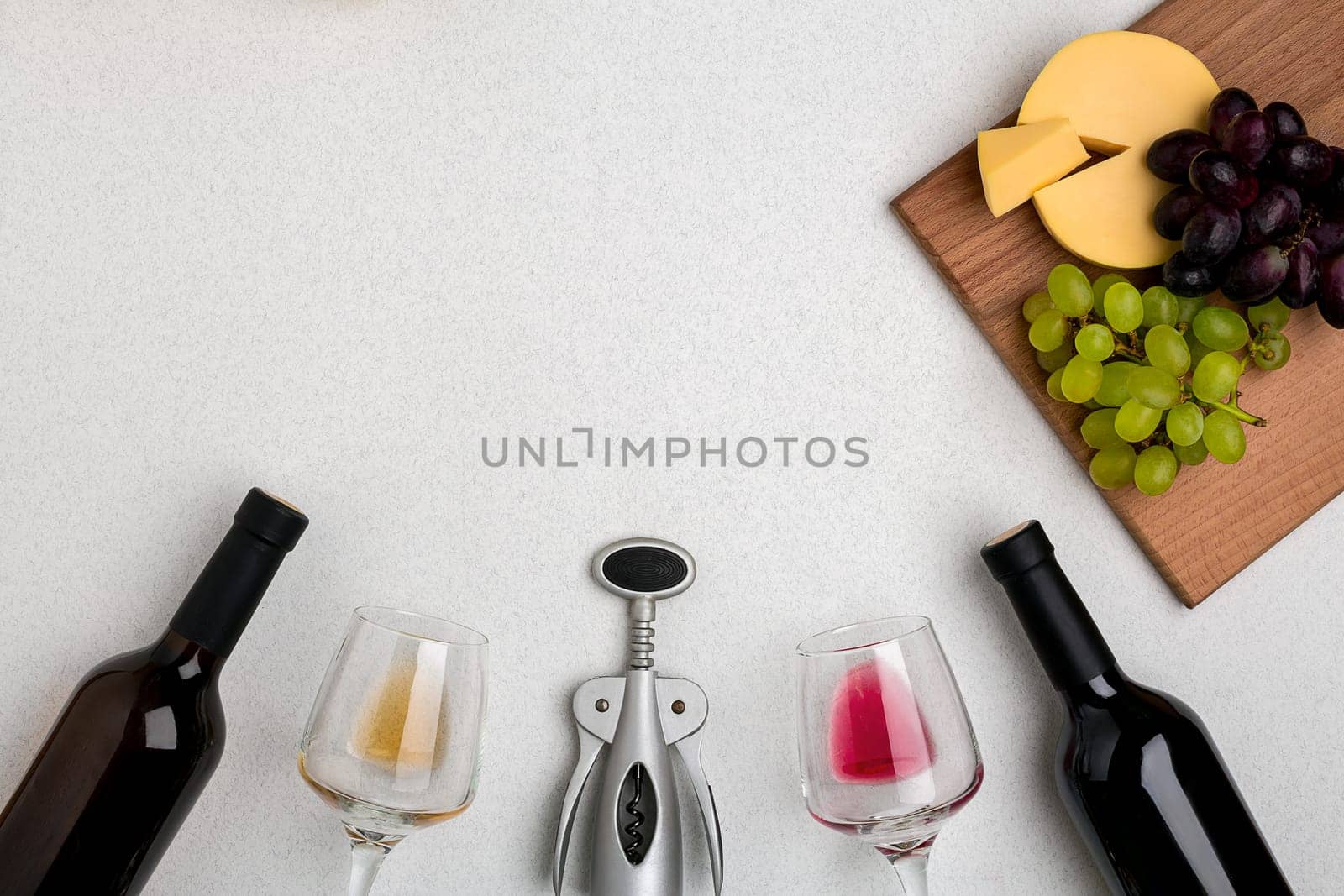 Two glasses of white and red wine, cheese and grapes. Two bottles of wine and a corkscrew. Top view with copy space