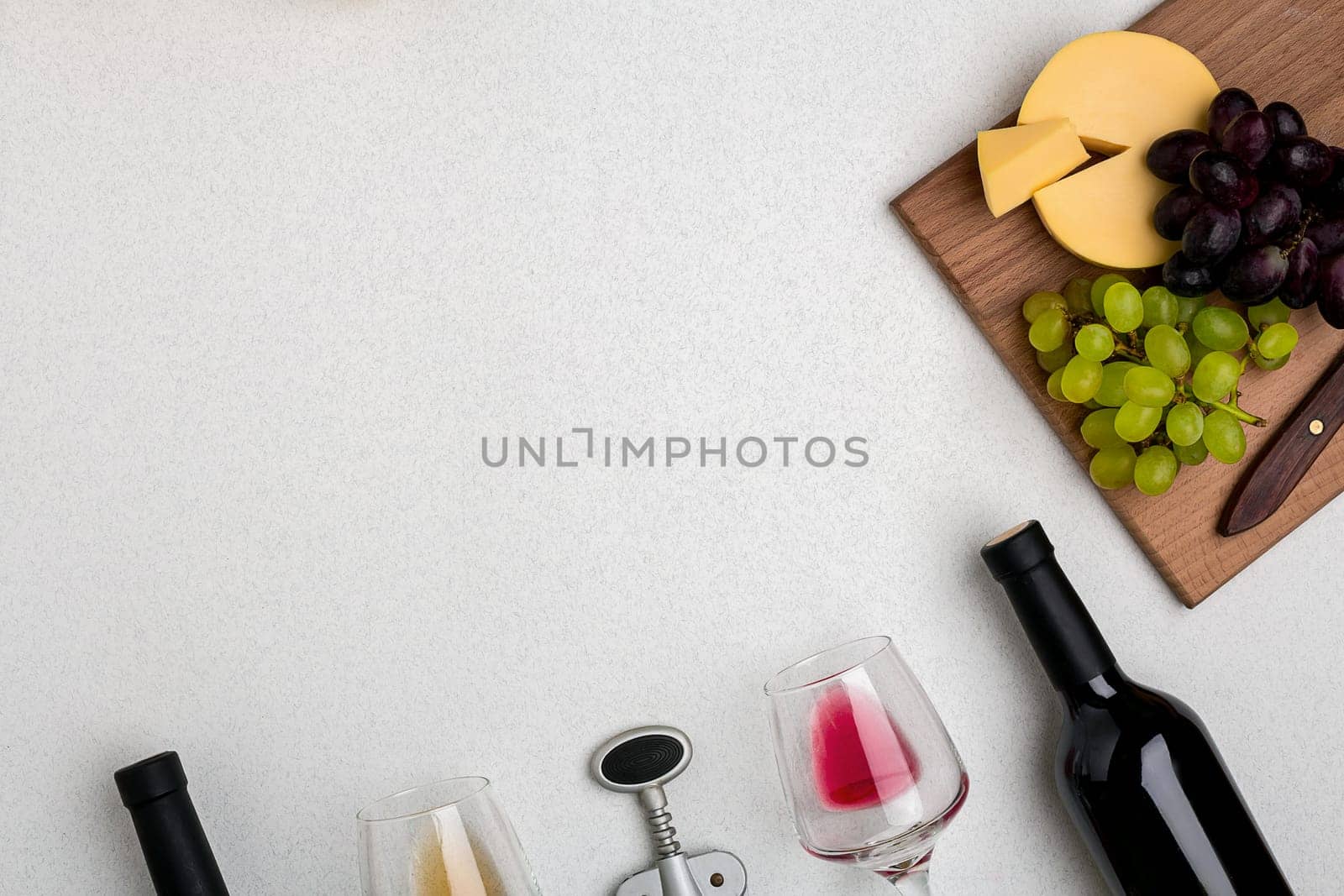 Two glasses of white and red wine, cheese and grapes. Two bottles of wine and a corkscrew. Top view with copy space