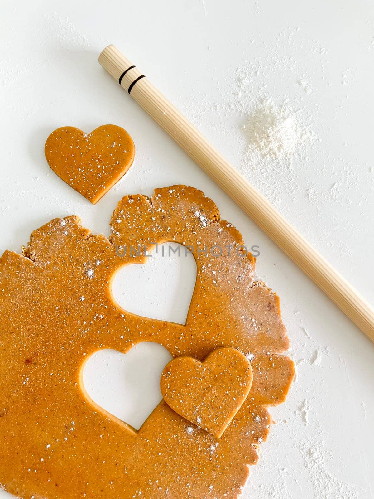 The process of cooking heart cookies. Top view of raw dough, rolling pin and baking cutter