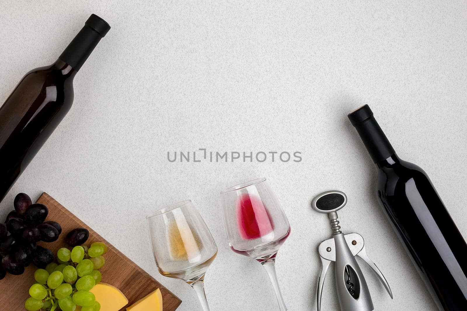 Two glasses of white and red wine, cheese and grapes. Two bottles of wine and a corkscrew. Top view with copy space